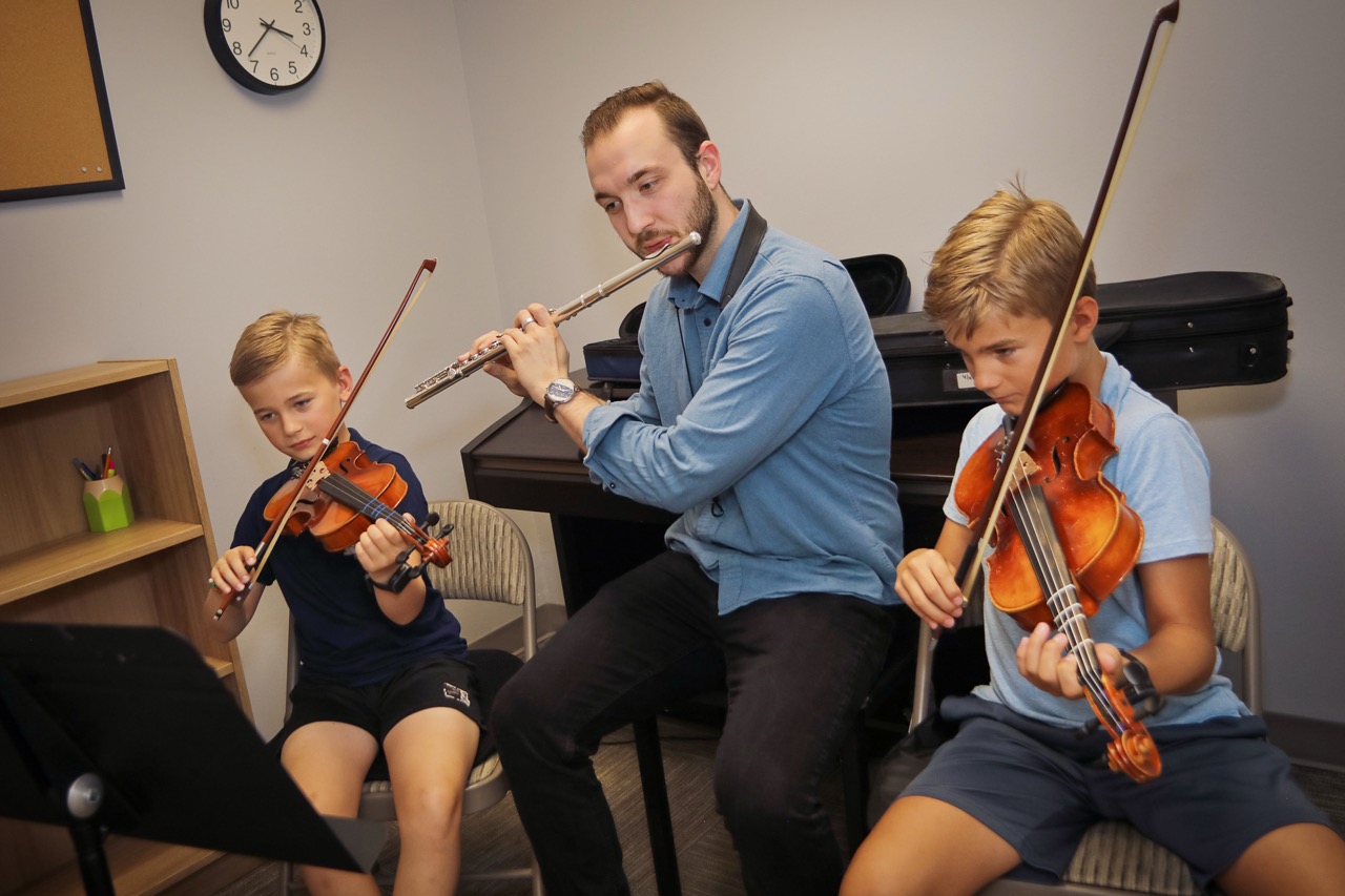 teacher playing flute with two violin students