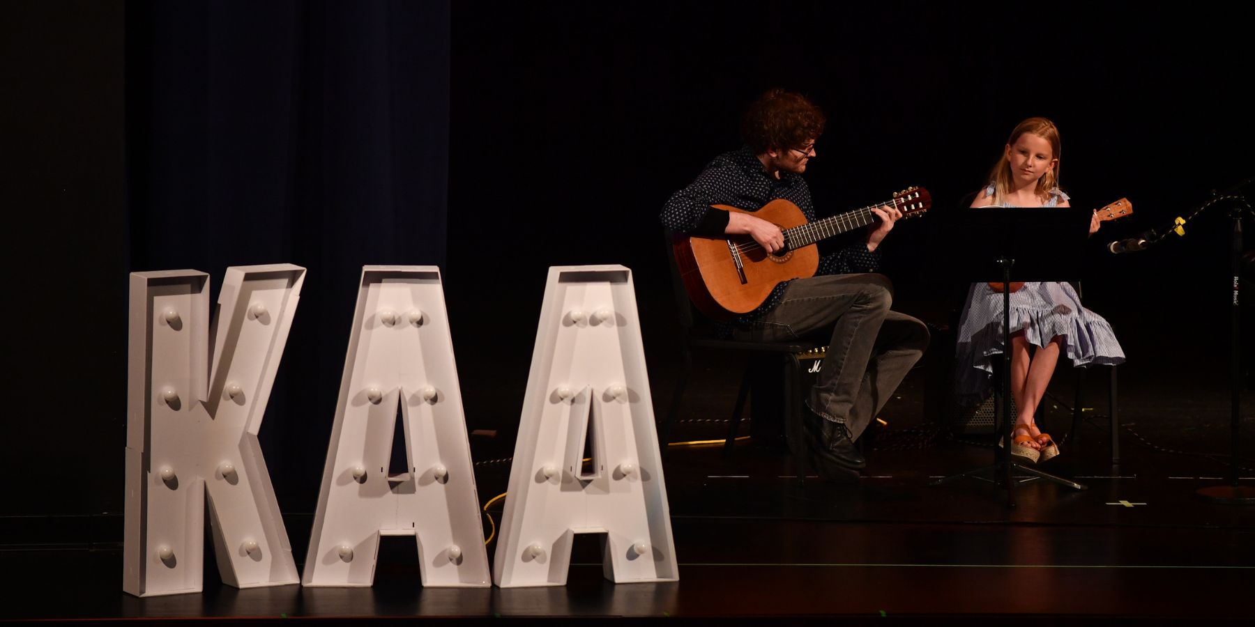 the KAA marquee sign on stage with two guitar players
