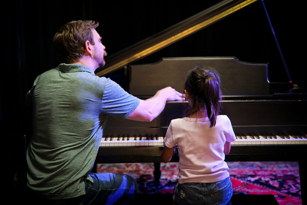 Piano teacher seated next to a young student teaching her how to play