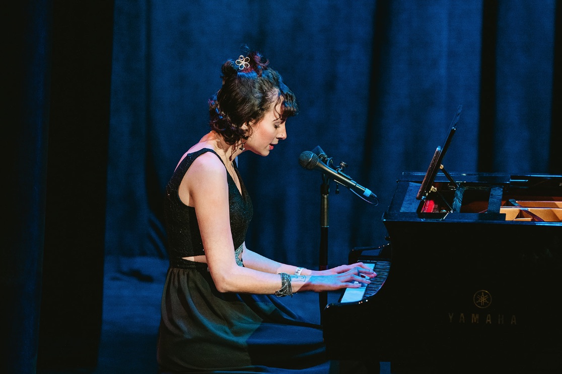 girl playing piano and singing into microphone